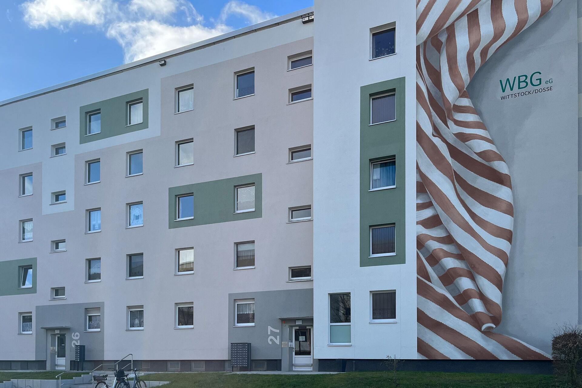 Grau Weißes 5 Geschosswohnhaus. Von der WBG eG Wittstock/Dosse steh am Gebäude.