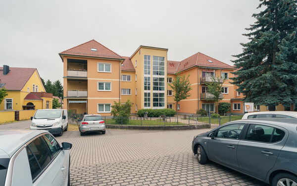 Parkplatz, parkende Autos, ein orangenes Gebäude mit Vorgarten.