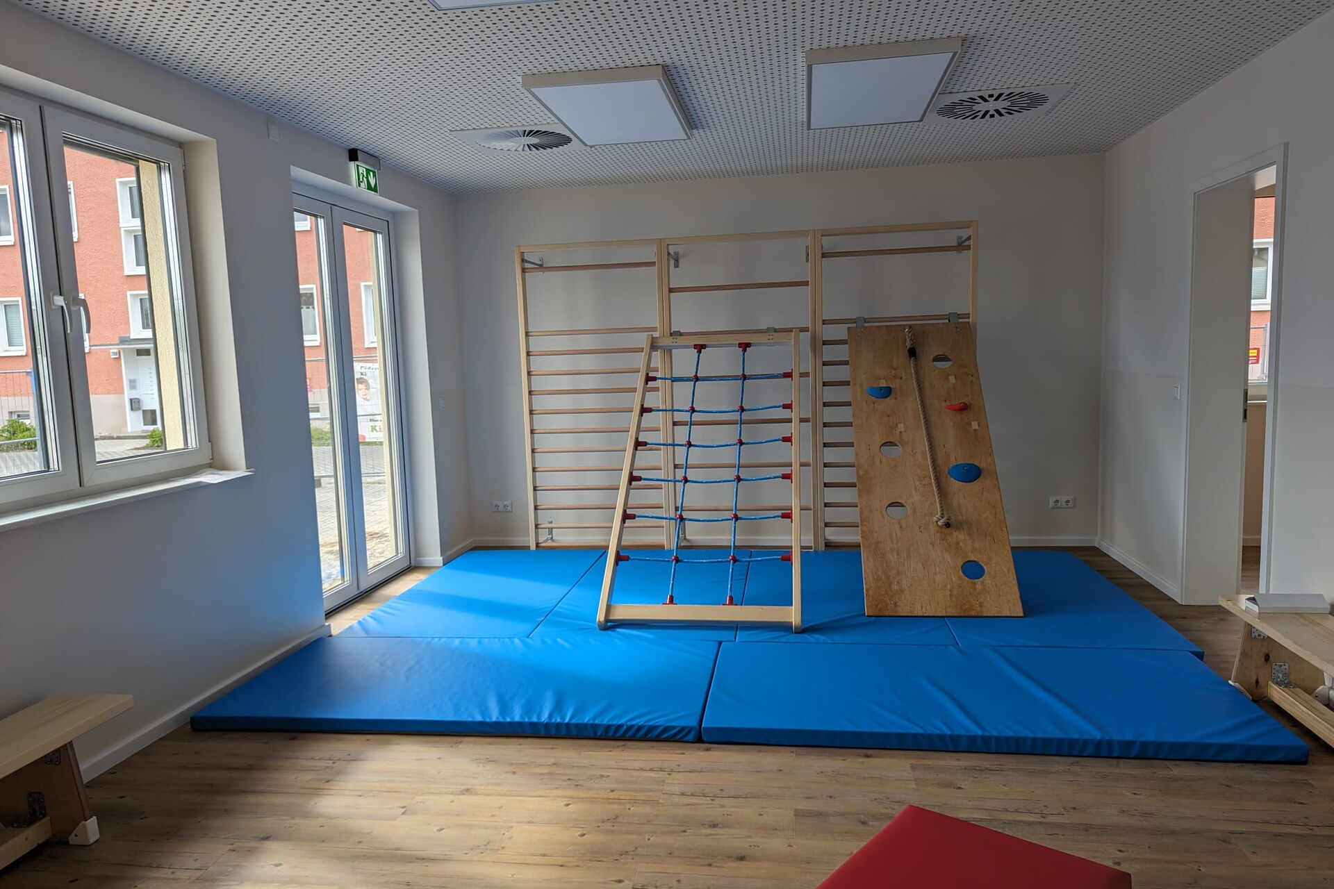 Sportraum. Große blaue Matten liegen vor eine Sprossenwand. An der Sprossenwand lehnen schräg zum rauf klettern zwei Kletterbretter.