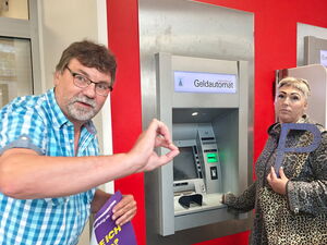 Eine Frau steht an einem Geldautomaten und hält ein großes P vor sich.