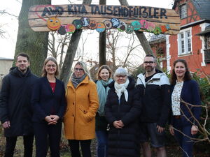 Gruppenbild: 5 Frauen und 2 Männer stehen draußen unter einem großen Holzschid mit der Aufschrift: "AWO Kita Tausendfüßler".