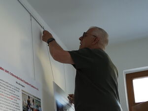 2 Männer, einer auf einer Leiter befestigen dritte Schaufatel rechts an einer Schiene an der Wand.