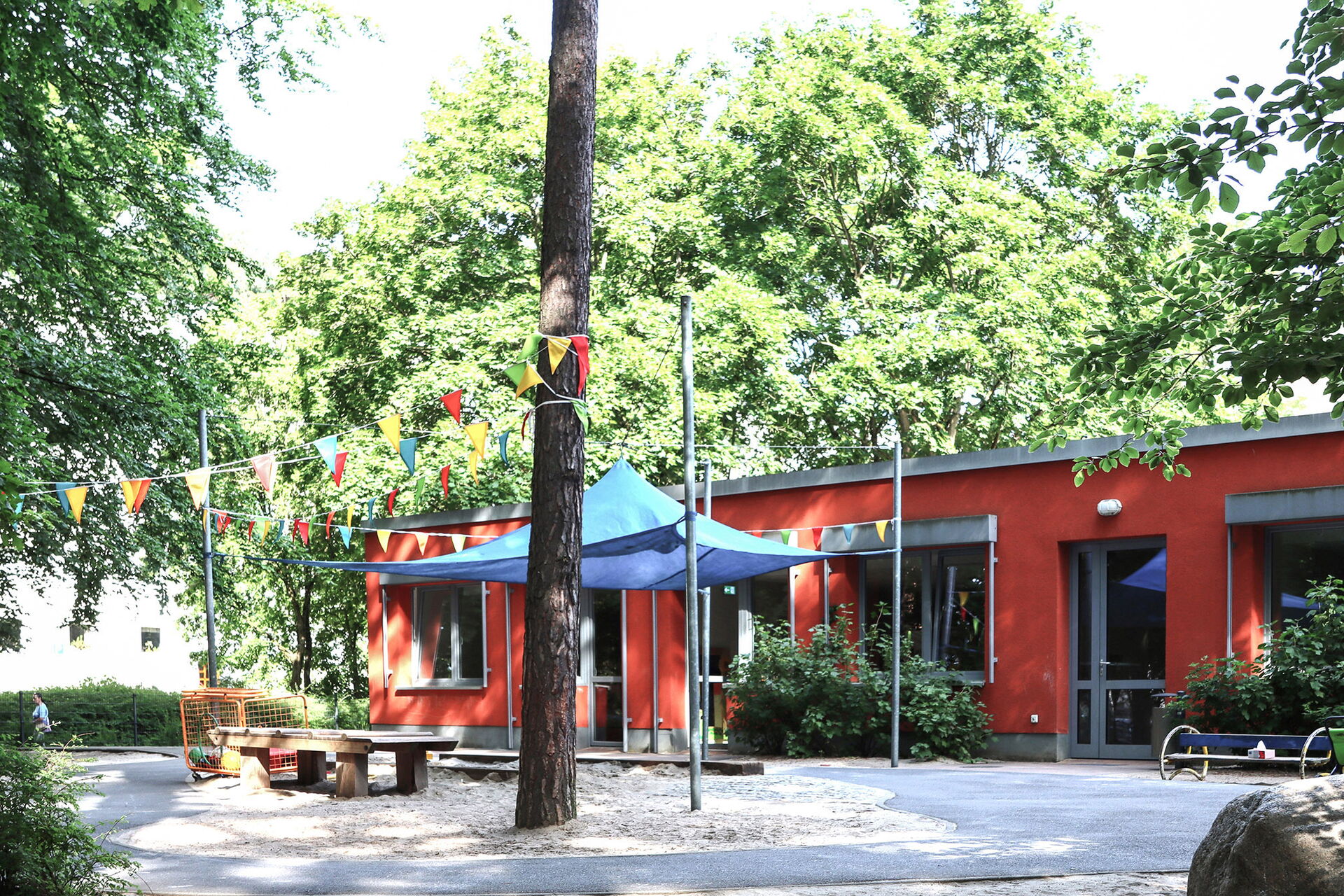 Spielplatz vor rotem flachen Kita Gebäude.