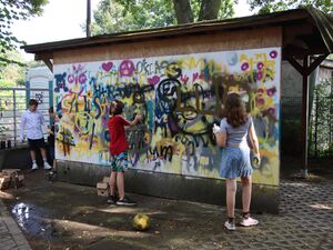 Zwei Mädchen ist kurzen Hosen und T-Shirts sprayen auf eine Graffiti-Wand.