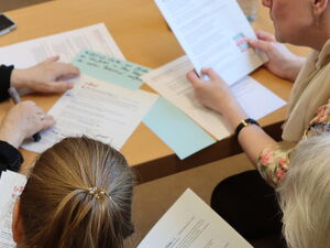 4 Personen lesen und bearbeiten Unterlagen an einem Tisch.