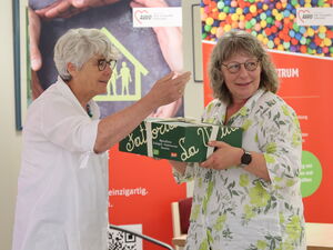 2 Frauen. Es wird ein Geschenk überreicht.