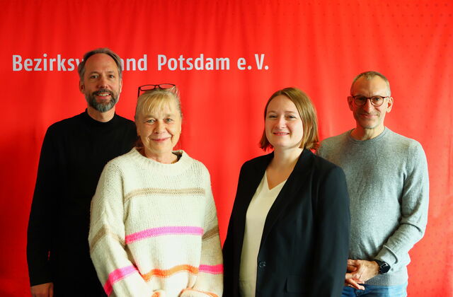 Gruppenfoto vor roter Wand. Zwei Männer hinten außen zwei Frauen vorne mittig. Alle lächeln in die Kamera.
