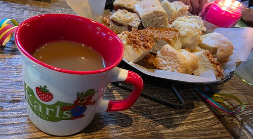 Kaffee in einer Tasse vom Karls Erlebnishof und ein Teller mit Kuchenstücken.
