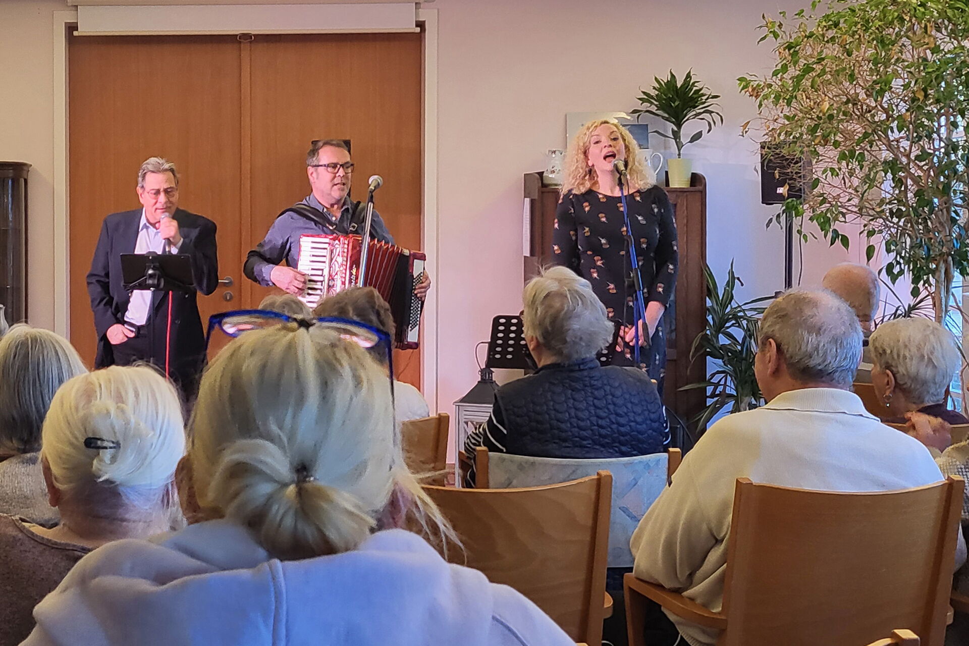 Ein Konzert. Bewohner sintzen auf Stühlen. Die Musiker und eine Sängerin stehen für dem Publikum.