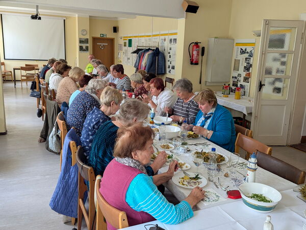 Großer Raum, lange Tafel in T-Form. Menschen essen Matjesgericht.