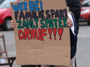 Eine Person hält eine beschriebene Pappe hoch. Auf dem Schild steht: "Wer bei Familien spart, zahlt später drauf".