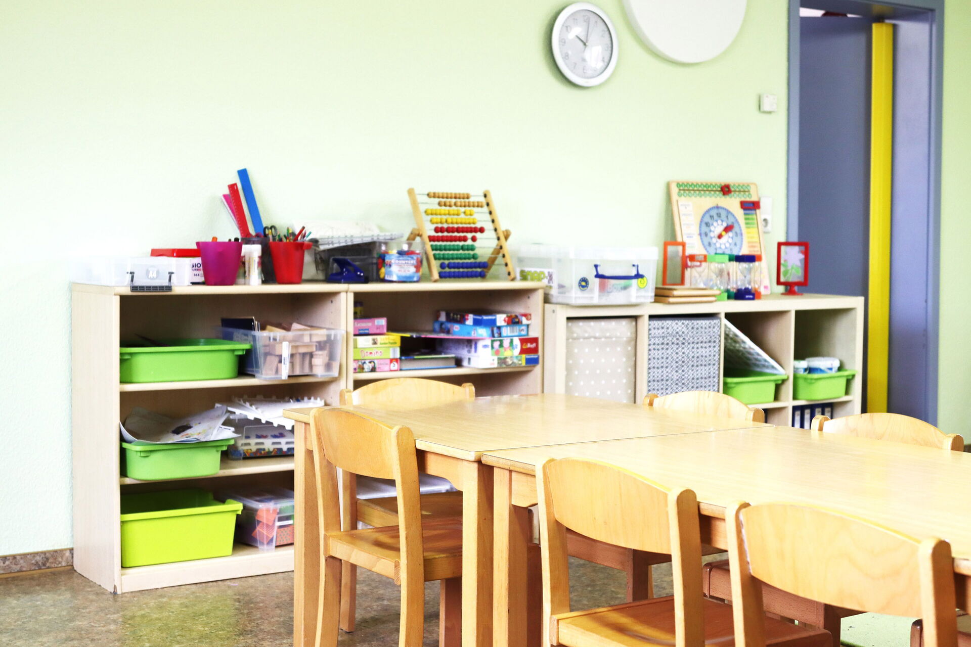 Spielzimmer. Raum mit hellen Wänden. Regale stehen an der Wand. Brettspiele sind im Regal. Auf dem Regal: Rechenschieber, eine Lernuhr und anderen Dinge.