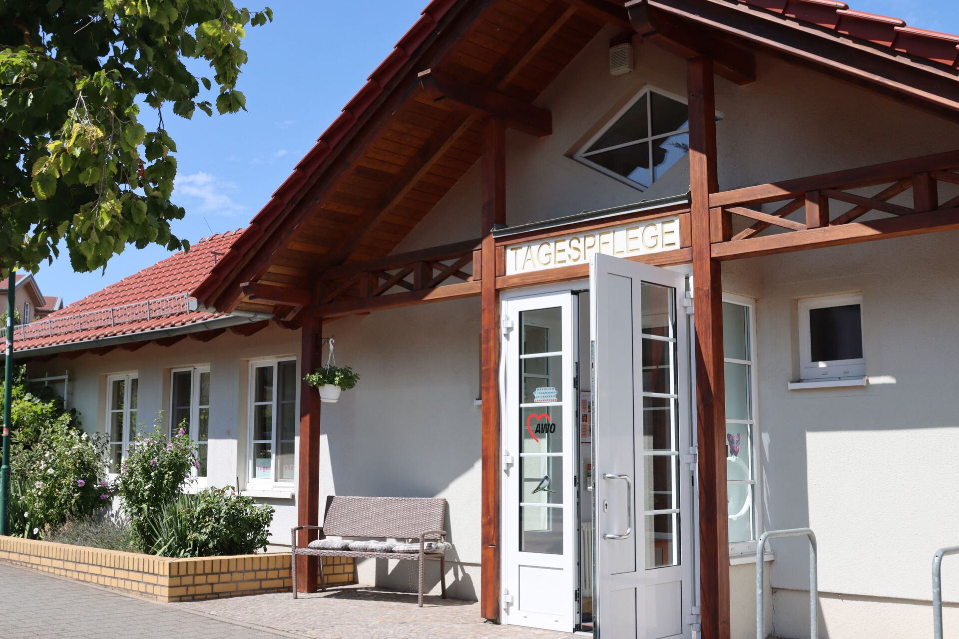 Sonne scheint auf den Eingang der Tagespflege eine Sitzbank mit Kissen steht draußen neben der Tür.