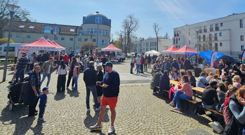 Totale. Ganzer Platz. AWO-Pavillons sind verteilt, Menschen sitzen recht im Bild auf Bänken, sonst frohes Markttreiben.