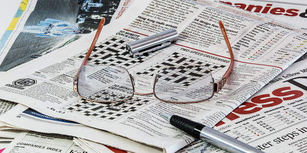 Hier sehen sie mehrere Zeitungen mit einer Brille und einem Stift darauf liegend