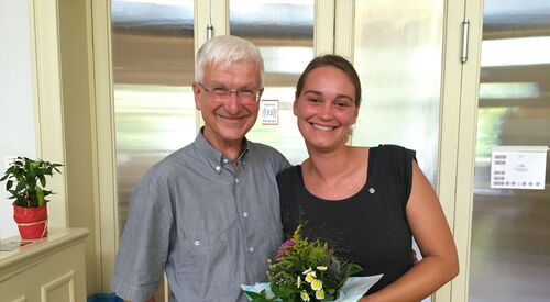 Auf dem Bild stehen Detlef Fronhöfer von der AOK und Anke Polkowski von der AWO Selbsthilfe Kontaktstelle Potsdam Mittelmark nebeneinander. Frau Polkowski hält einen Blumenstrauß in der Hand. Beide lächeln in die Kamera.