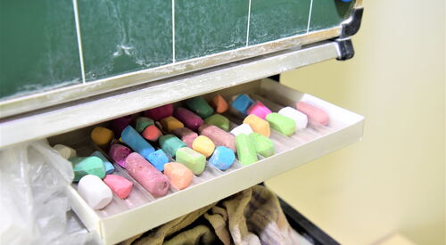 Schultafel. Kreidefach. Mit vielen Kreidestücken und verschiedenen Farben: Grün, Gelb, Blau, Weiß, Rot.