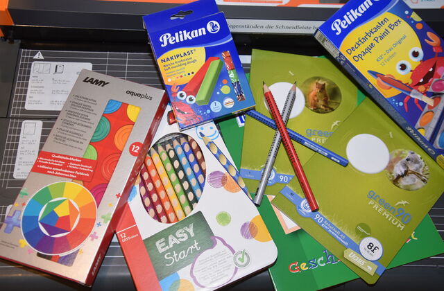 Schulmaterial. Eine Packung mit Buntstiften, Pelikan Knete Nakiplast, Deckfarbkasten von Pelikan, Wasserfarbkasten von LAMY Aquaplus, Schulheft Staufen Recycling green90 Premium