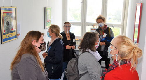 Frauen in einem Raum mit Bildern an der Wand. Frauen tragen OP- Und Stoffmasken