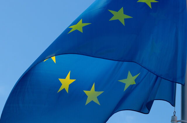 Blaue Flagge der Europäischen Union mit gelben Sternen, wehend vor blauem Himmel.