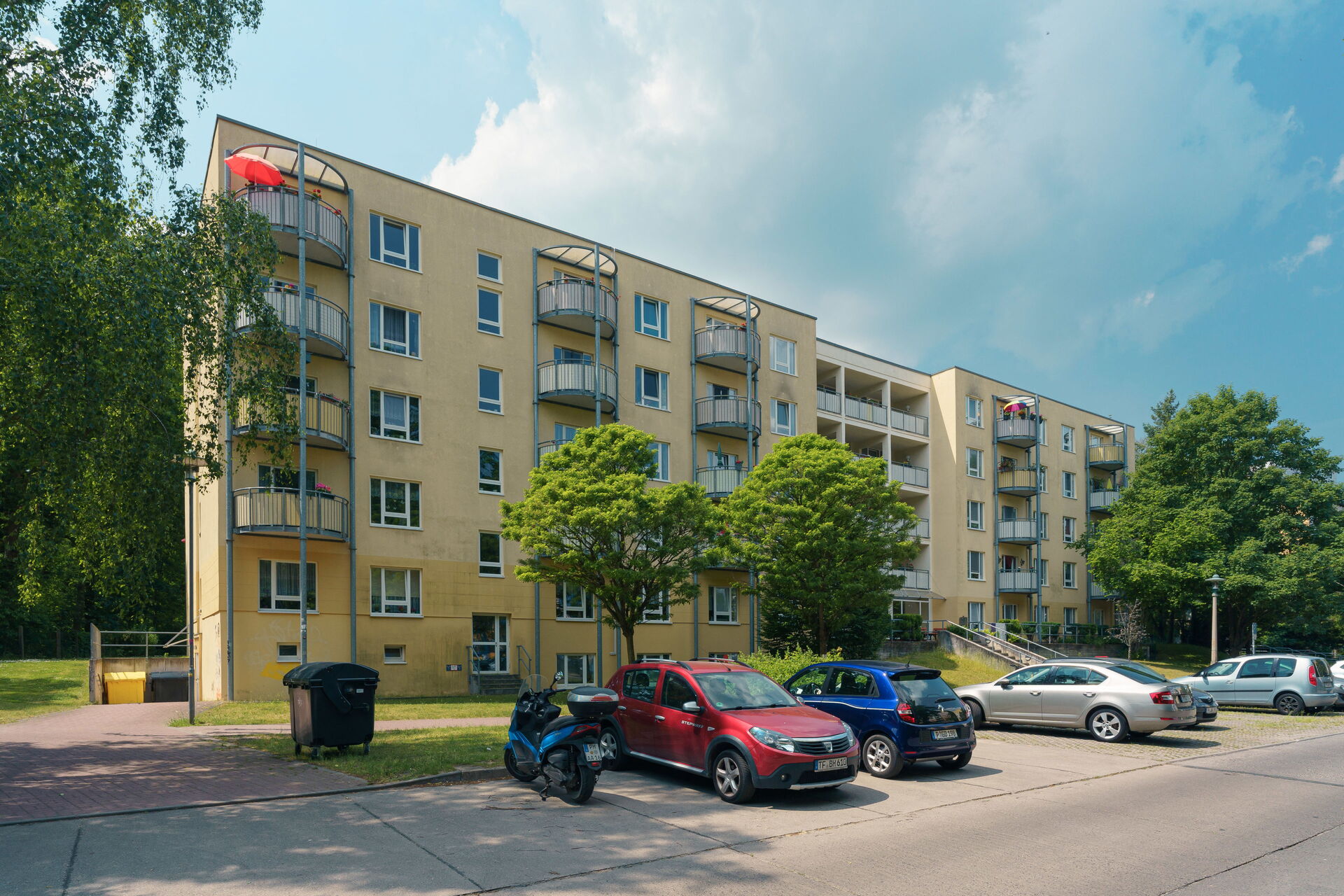 Großes Wohnhaus mit hellgelber Fassade und davor parkenden Autos.