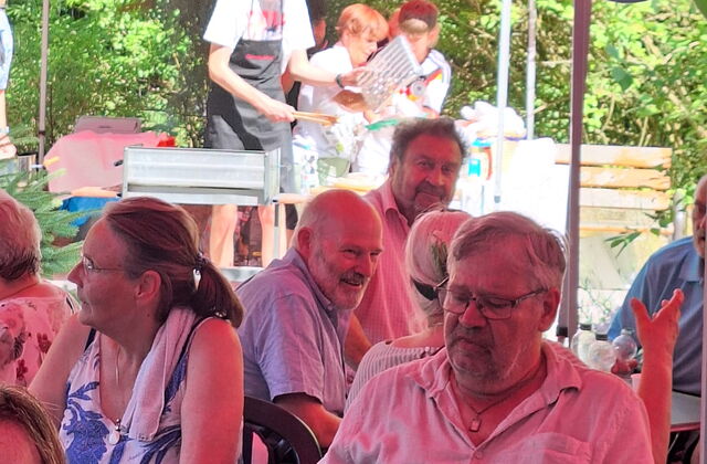 Mehrere Menschen sitzen im Schatten unter Pavillons.