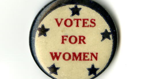 Zu sehen ist eine Art Button mit der roten Aufschrift Votes for Women. Es sind fünf blaue Sterne auf dem Button zu erkennen