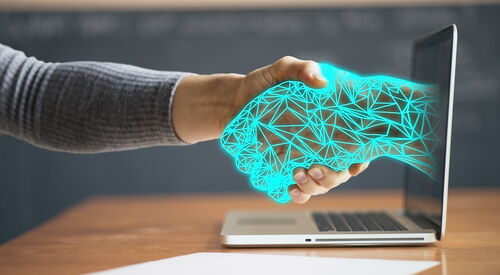 Laptop auf einem Tisch, aus dem Bildschirm ragt eine leuchtend blaue Cyber-Hand heraus und schüttelt eine menschliche Hand, die von links entgegen gestreckt wird.