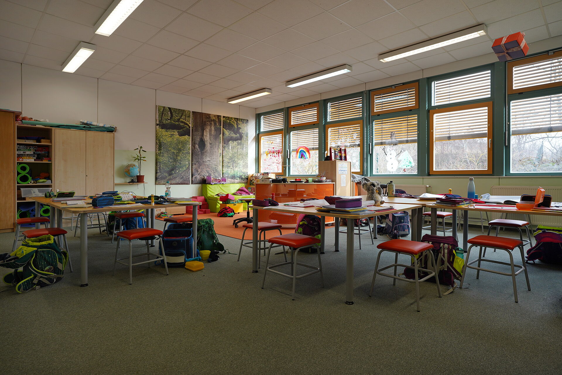Lernzimmers. Mehrere Tische mit Hockern im Raum verteilt. Auf den Tischen liegen Federmappen und Blöcke, An den Tischen stehen Schulmappen auf dem Boden. Großer Raum.