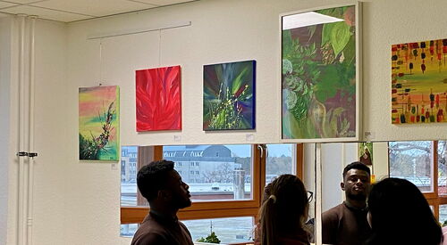 5 Bilder an einer Wand. 3 Besucher schauen sich die Bilder an.