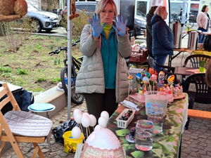 Stand zum Ostereier bemalen. Vorne auf einem Tisch viele farbige Ostereier. Eine Frau im Stand zeigt ihre bunten behandschuhten Hände.