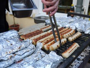 Ein Grill mit Grillwurst, die mit der Grillzange gewendet werden.