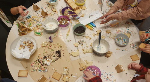 Weihnachtsplätzchen dekorieren. Runder Tisch von oben. Plätzchen, Glasuren, bunte Streusel. Kinderhände die mit dekorieren beschäftigt sind.