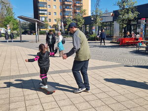 Mädchen auf einem Skateboard.  Mann läuft nebenher und passt auf.