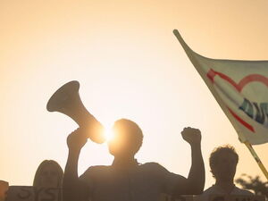 eine Gruppe Menschen demonstriert, eine AWO-Flagge schwingt im Wind. Im Hintergrund geht die Sonne unter.