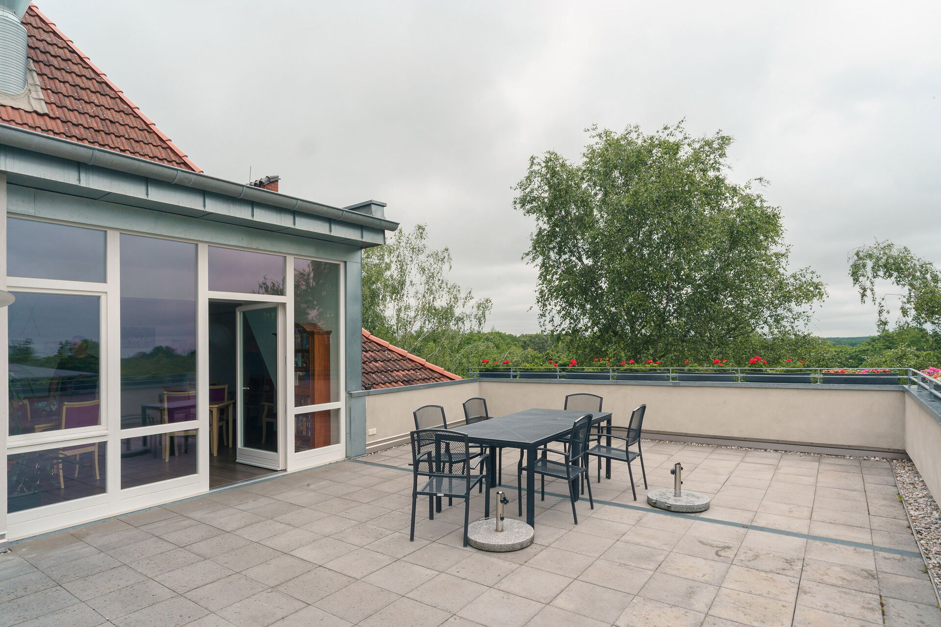 Große Dachterrasse mit Tisch, 6 Stühlen. Terrassentür steht offen, Glasfront.