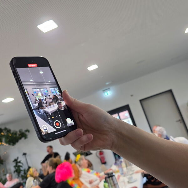 Ausgestreckter Arm hält ein Smartphone und filmt die Feier.