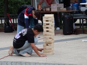 Zwei Jungs am Jenga-Turm. Einer ist auf die Knie gegangen und versucht einen Holzklotz zu entnehmen.