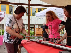 Eine Frau versucht sich am Spiel "heißer Draht". Mit einem Stock an dem ein Ring ist, fähr man an Draht oder Rohren entlang darf diese aber nicht berühren.