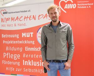 Portrait: Mann mit blonden Lockenkopf, Dreitagebart. Er trägt T-Shirt, Jacke, Jeans, die Daumen lässsig in den Hosentaschen verhakt
