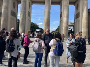 Gruppe. 7 Frauen, ein Mann stehen vor dem Brandenburger Tor in Berlin. Die Frauen haben Rucksäcke auf.