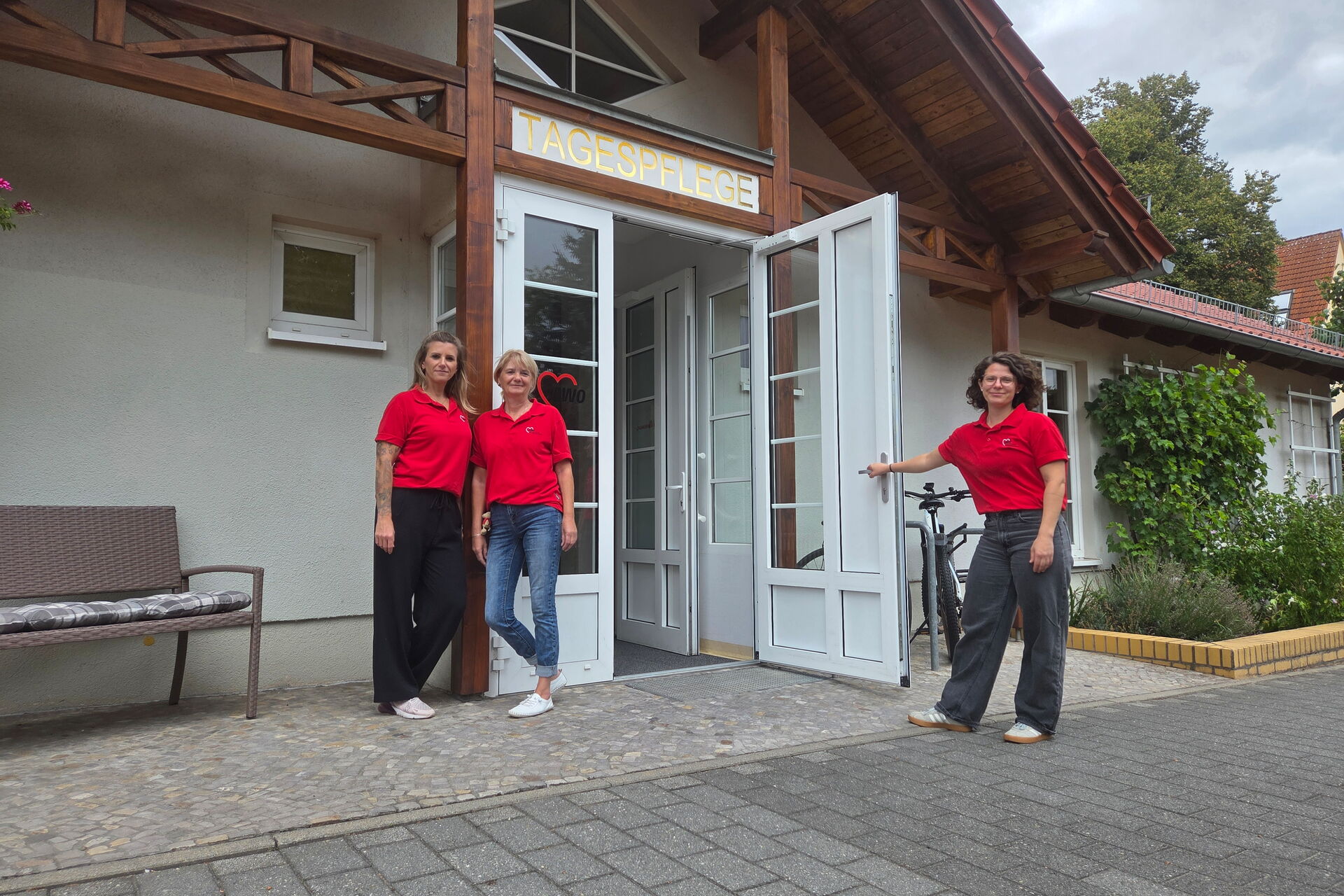 3 Pflegerinnen in roten T-Shirts vor dem Eingang zur Tagespflege.
