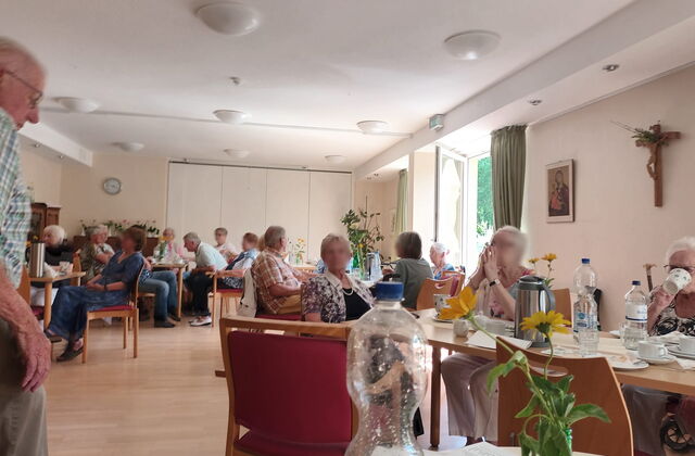 Raum, mehreren Tischen an denen Menschen sitzen. Kaffee und Wasserflaschen auf den Tischen.