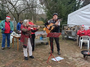 Musikprogramm im Freien mit kleiner Feuerschale. Frau miit Geige, Mann mit Gitarre Notenständer steht vor ihnen.