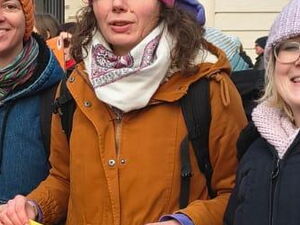 Frauen halten ein orangenes Band. 3 Frauen im Vordergrund mit orangenem Luftballon und einem Schild in den Händen. Text: Wo ist die Ministerin?