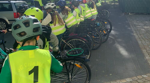 Kinder in gelben Warnwesten mit Fahrrad und Fahrradhelm stehen auf einem Parkplatz.