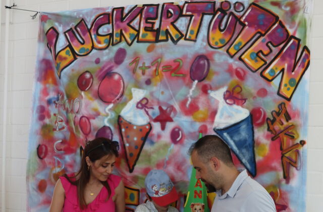 Frau, Kind mit leerer Zuckertüte und mann, vor einem großen Transperen mit Zuckertüten und dem Schriftzug oben drüber.