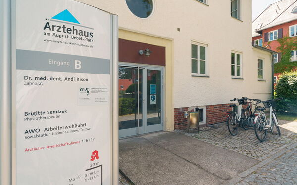 Eingang vom Ärztehaus, ohne Stufen. Schild vom Ärztehaus steht draußen links neben dem Eingang.