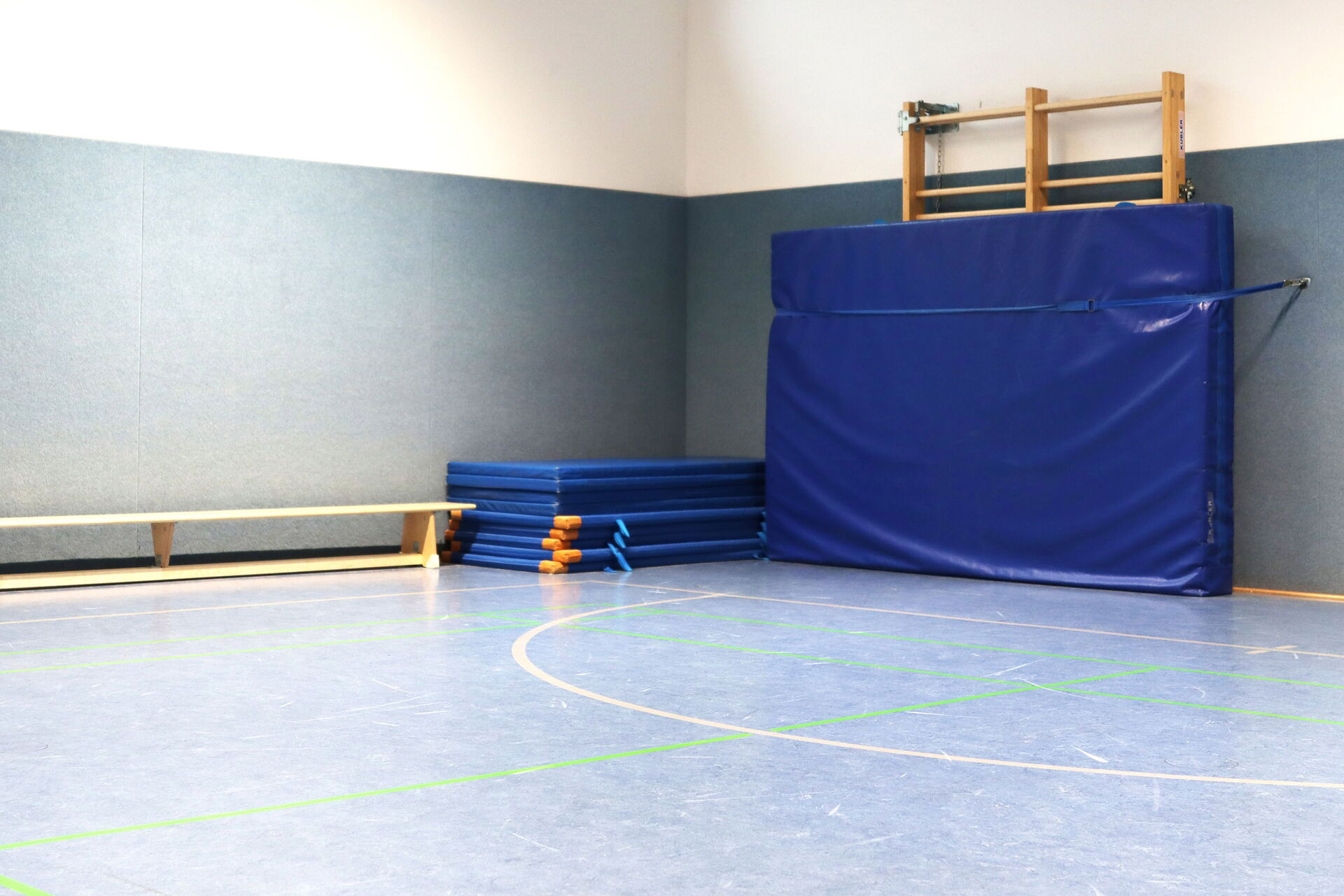 Turmhalle, an der Wand steht eine Sitzbank. Vor der Sprossenwand ist eine große blaue Weichbodenmatte gespannt.