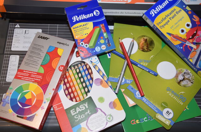 Schulmaterial. Eine Packung mit Buntstiften, Pelikan Knete Nakiplast, Deckfarbkasten von Pelikan, Wasserfarbkasten von LAMY Aquaplus, Schulheft Staufen Recycling green90 Premium
